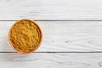 Curry powder in wooden bowl on white wooden background with copy space