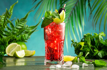 Red alcoholic cocktail with bitter, whiskey, soda, lime, mint and ice. Dark tropical background,...