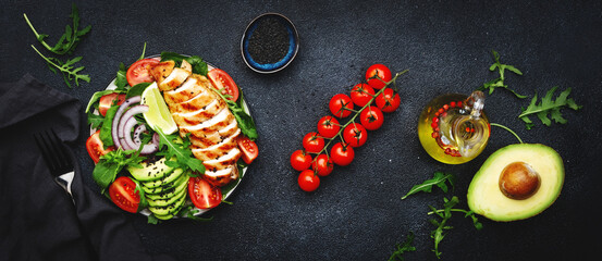 Fresh vegetable salad with grilled chicken fillet, spinach, tomatoes, avocado, sesame seed and red onion on black background.. Healthy, detox, ketogenic diet food.. Top view banner