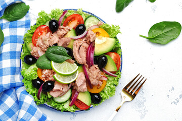 Tuna fish salad with avocado, tomato, cucumber, black olives, spinach, red onion and lettuce. White stone background, top view
