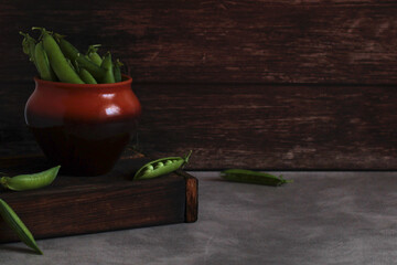 fresh pea pods in a clay pot on a wooden box