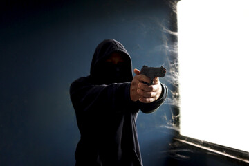 Criminal man in black hood holding a gun pointing victim, Mask thief robber with his gun on hands...
