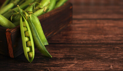 fresh pea pods with peas in a wooden box on a wooden background
