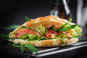 Croissants with salted salmon, cucumber and arugula served on dark background. Close up.