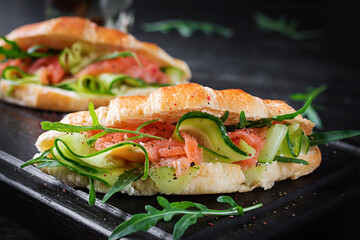 Croissants with salted salmon, cucumber and arugula served on dark background. Close up.