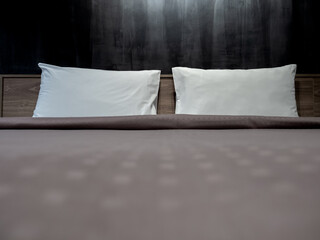 Fototapeta na wymiar Couple white pillow on the empty bed with brown duvet on dark grunge concrete wall background, loft style in hotel bedroom. Two soft and clean comfort pillows preparing for the guest in the resort.