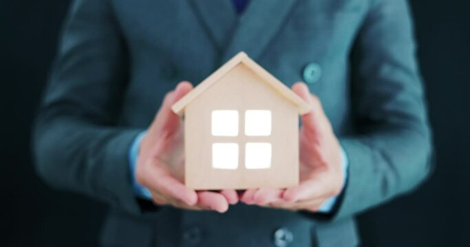 Businessman, agent or broker at front. To hold model of home, house or residential building in hand and offer to sale, rent buy, purchase and investment. Concept for business, real estate, property.