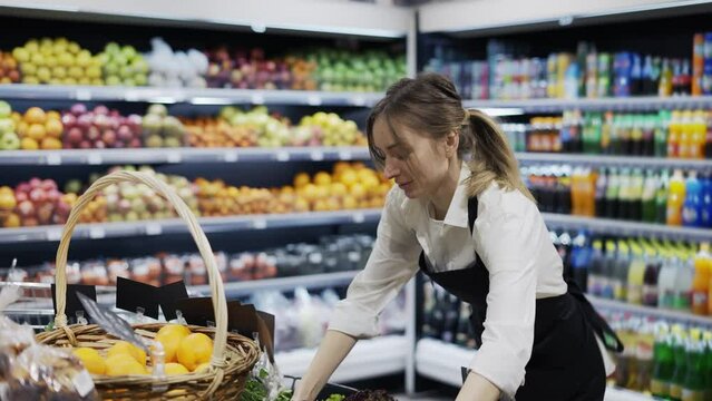 a girl worker in a black apron puts a box of greens on a shelf. Work days. Healthy food