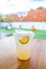 Honey Lemon Soda with lemon slices put in a plastic cup placed on a brown wooden table wood in the playground