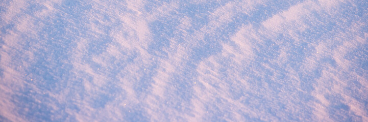 Beautiful winter background with snowy ground. Natural snow texture. Wind sculpted patterns on snow surface. Wide panoramic texture for background and design.