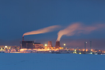 Naklejka na ściany i meble Night industrial landscape. View of a large thermal power plant and snow-covered tundra. Cold winter weather. Severe polar climate in the Arctic region. Industry and energy in the Far North of Russia.
