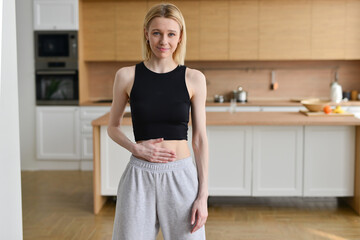 Hungry slom woman on diet stands in kitchen and touches her belly
