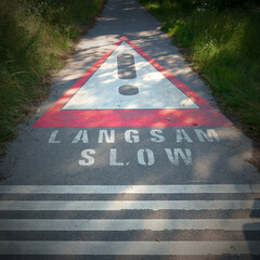 Aufforderung zum langsamen Fahren in deutscher und englischer Sprache auf einer engen asphaltierten...