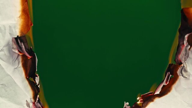 White paper burns from above on a green background copy space. The sheet of paper burns and reveals a green background for pasting.