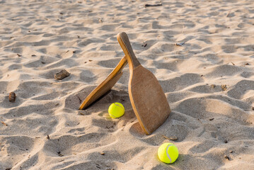 Two wooden rackets and tennis balls in a golden sandy beach on a beautiful summer day.