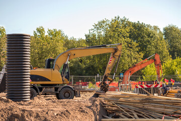 Yellow road crane on a gravel construction site with a blue sky and green trees in the background