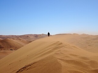 Fototapeta na wymiar lone man walking on top of a sand dune in the Namib desert in Namibia