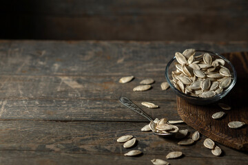 Pumpkin seeds in a glass saucer on a wooden background.