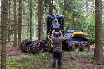 Man stands in forest and wants to stop timber harvester as it destroys forest floor