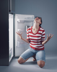 Desperate hungry woman and empty fridge