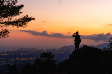 Landscape, silhouette of a boy on a rock photographing the landscape at sunset