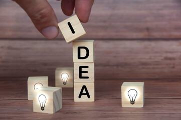 Idea text on wooden blocks surrounded by light bulbs on wooden background. Business idea concept