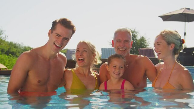 Portrait of smiling multi-generation family on summer holiday relaxing and splashing in swimming pool - shot in slow motion