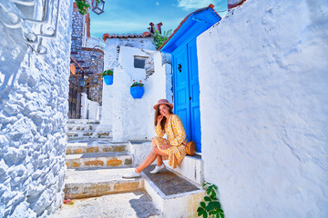 Girl traveler wearing dress and hat walks on an old beautiful street with white houses and blue doors in a European city