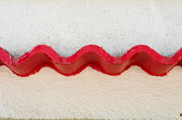 Una piccola tettoia ondulata e dipinta di rosso sul muro bianco di una casa