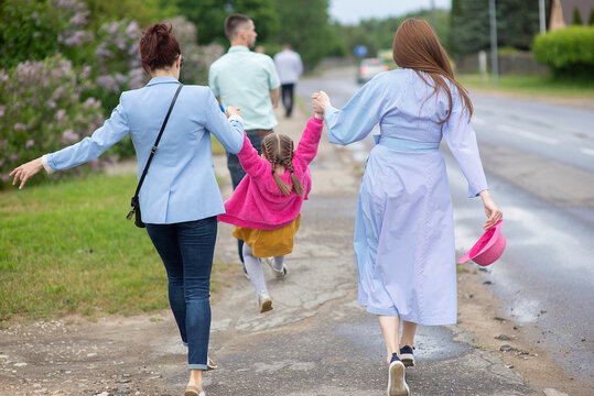Rear view of two female mothers sisters going for a walk and carrying a little girl in pink clothes