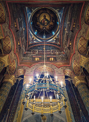 Fototapeta na wymiar Interior architectural details of the Curtea de Arges monastery. The hall with tall columns, christian Orthodox painted icons on walls and a golden chandelier with lights suspend out of ceiling