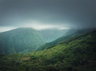 Beautiful view to the green hills in Hawaii, Oahu island. Hiking mountains landscape with vibrant tropical vegetation. Moody weather with foggy clouds over the valley