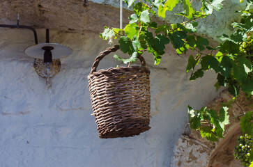 Un cesto di vimini appeso a una corda davanti al muro bianco di una masseria in Salento - obrazy, fototapety, plakaty