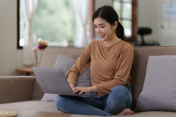 Asian woman checking social media by laptop sitting on sofa at home. lifestyle concept