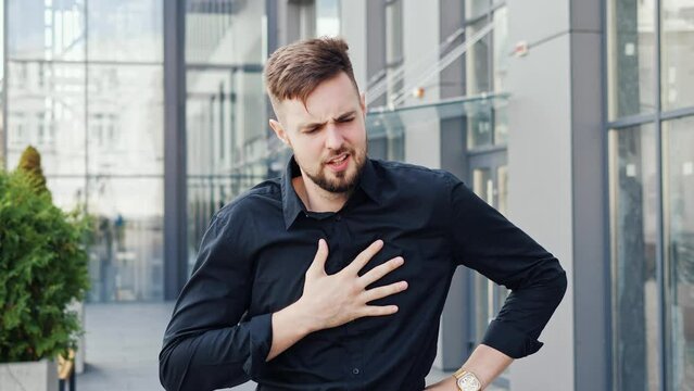 Pain in chest, handsome businessman fear symptoms with pain outdoor. A stressed man has panic attack with hard breathing, suffering heartache, risk of heart attack. Male entrepreneur, problem at work.
