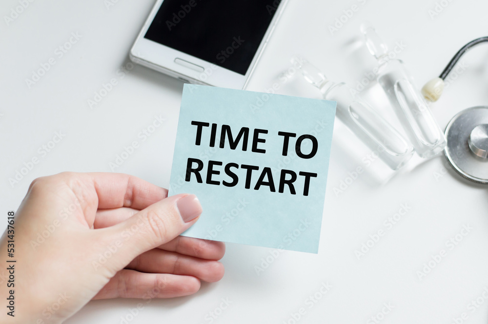 Poster time to restart text on a blue card in the doctor's hand against the background of a table with medi