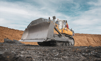 Yellow excavator in career moves overburden. Bulldozer combs the ground, with the bright sun and...