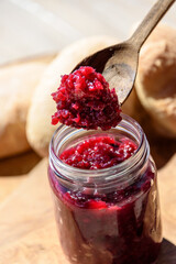 homemade red fruit jam, jar and wooden spoon with freshly baked bread tin the back