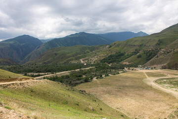 Dramatic landscape - the picturesque Baksan valley with a country road among the hills against the background of cloudy sky and foggy haze in the Elbrus region in the North Caucasus