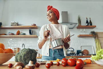 Beautiful African woman mixing something in pan and smiling while preparing food at the kitchen