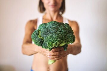 Fototapeta na wymiar young woman dressed in white t-shirt showing with broccoli. High quality photo