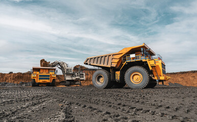 Obraz premium Large quarry dump truck and excavator. Big mining truck work coal deposit. Loading coal into body truck. Production useful minerals. Mining mining machinery to transport coal from open-pit production