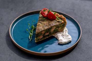 Round PIE with spinach and fish. Sliced Savory quiche with salmon and spinach, close-up on the plate. 