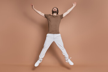 Fototapeta na wymiar Full length of happy young man jumping against brown background