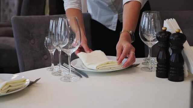 Shot of waiter female hand puts on cloth napkin on table before celebration at banquet hall. Banquet dinner. Elegant Wedding Empty Table with Glass in Restaurant.