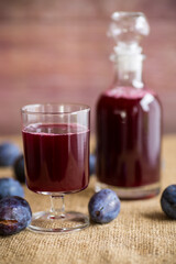 plum red wine in a glass and a decanter against the background of ripe large plums