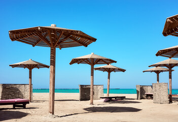 Wooden sun umbrellas, sunbed and windscreens on beach, Marsa Alam, Egypt.