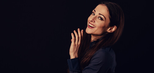 Beautiful thinking toothy laughing business woman with hand near the face in blue shirt on black background with empty copy space for text. Closeup