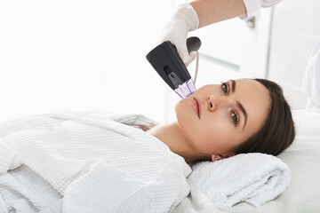 Obraz na płótnie Canvas Woman while RF lifting procedure for her face skin tightening with cosmetologist at a beauty salon