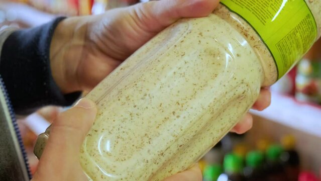 Close up of male hands holding product in plastic bottle to read ingredients details in store. Conscious shopping concept. 4k video